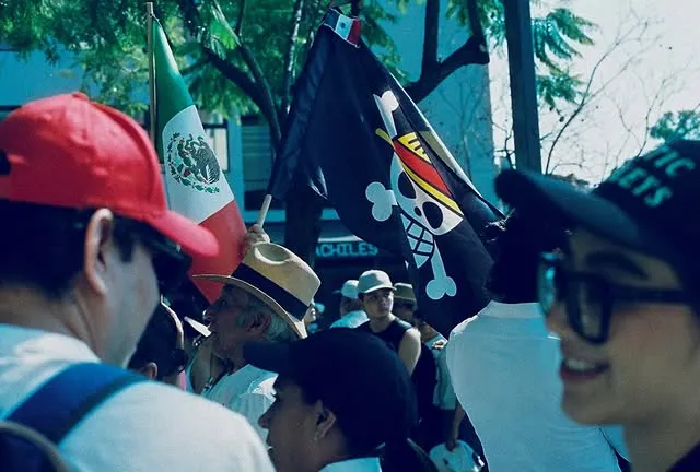 Personas en una marcha con la bandera de México y una bandera pirata