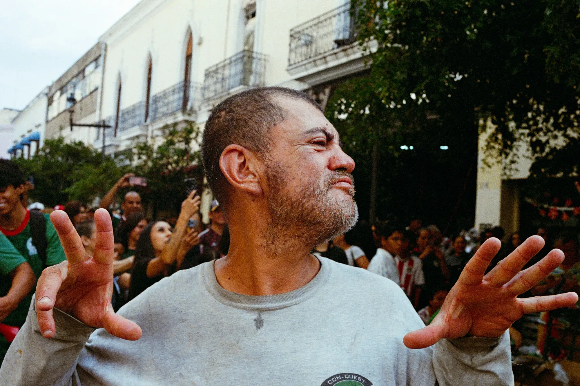 Hombre con los brazos abiertos y las manos en primer plano, entre una multitud en la calle